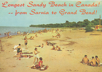 A vintage postcard shows sunbathers scattered across a wide sandy beach stretching between Sarnia and Grand Bend, advertised as "Canada's Longest Sandy Beach" in retro red lettering.