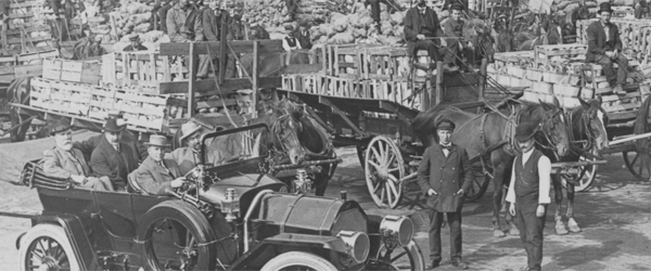 A car with many heavily loaded horse drawn wagons.