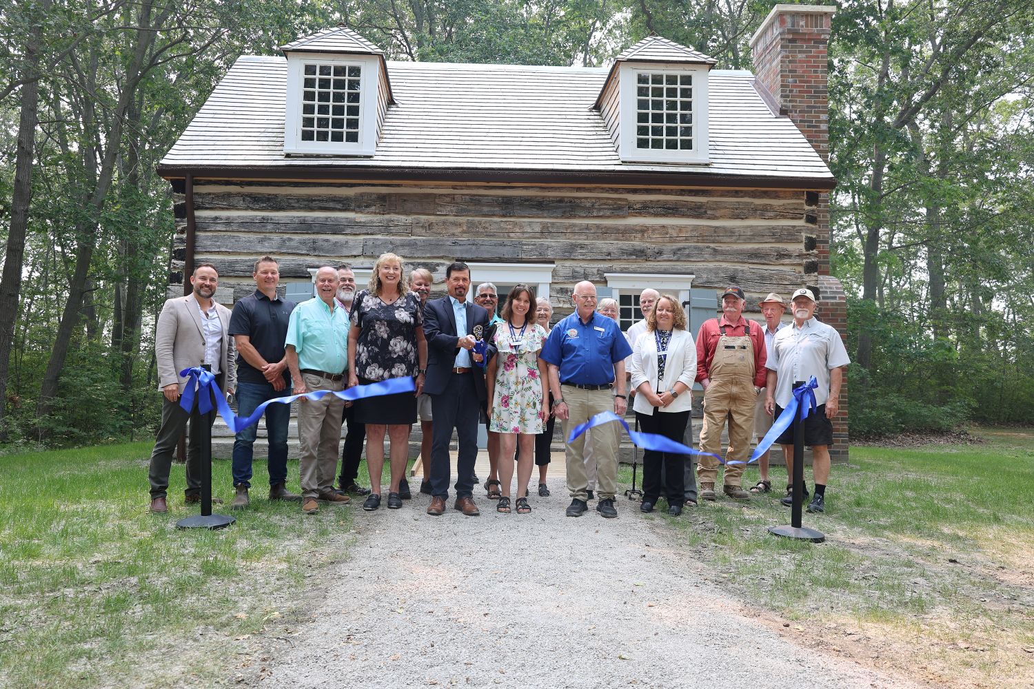 a group of people cuts a big ribbon outside a log cabin