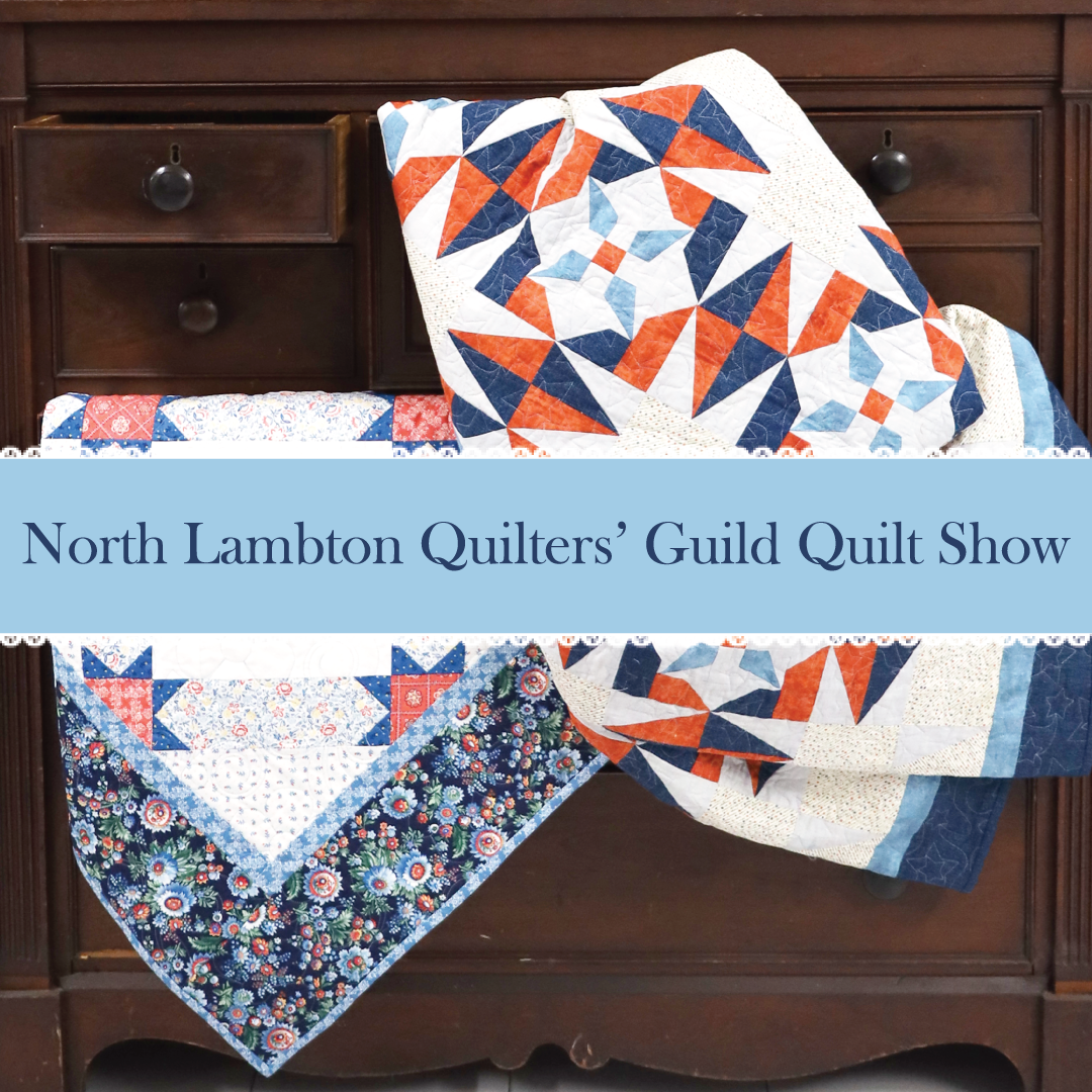 A dark dresser has two blue and orange quilts draped over the drawers. A light blue overlay with white lace reads "North Lambton Quilters' Guild Quilt Show'.