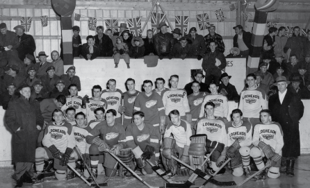 A black-and-white photo of a hockey team in an indoor rink with a crowd and flags in the background.