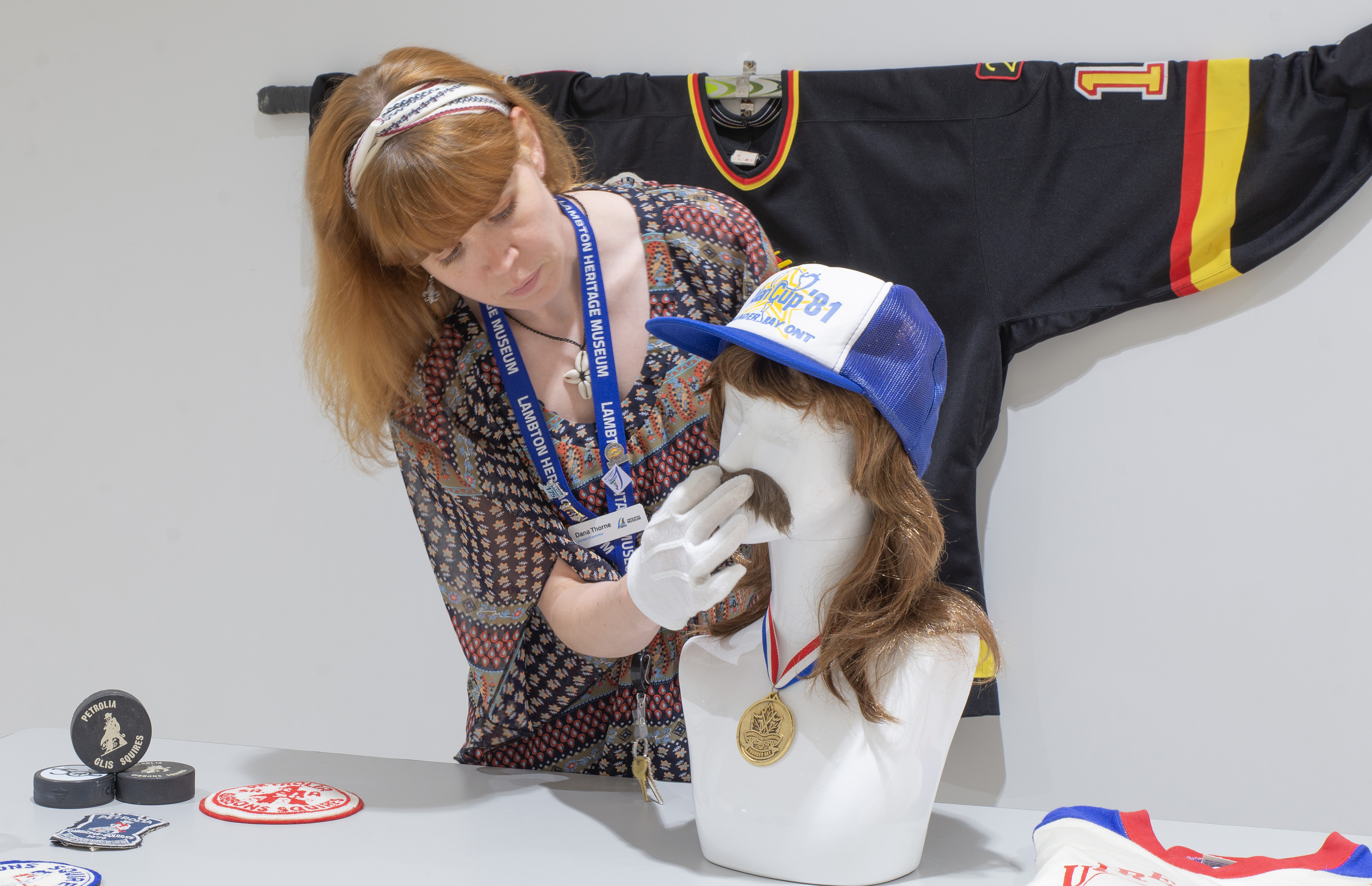 A white woman considers the placement of a moustache on a mannequin for a museum exhibit on hockey