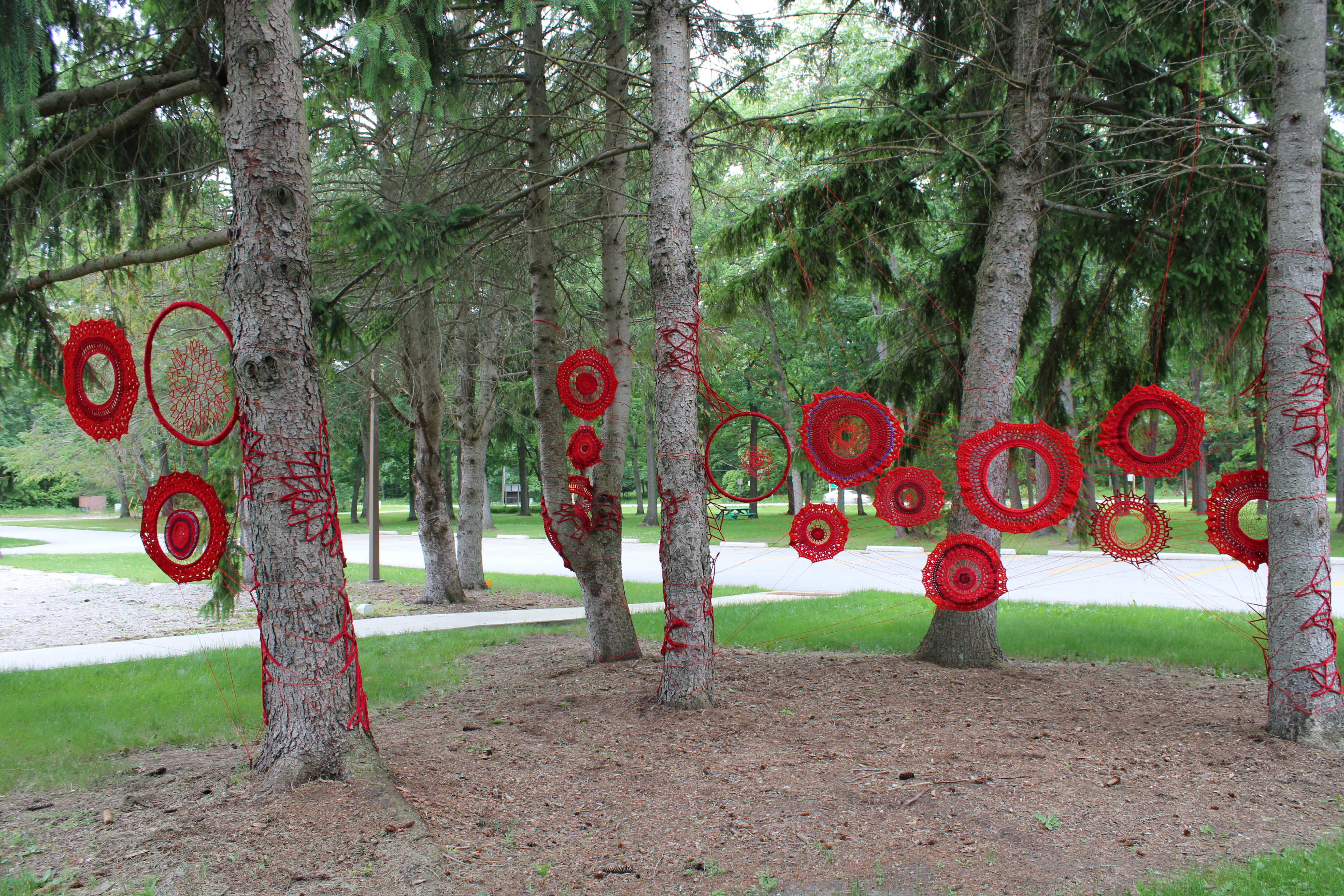 Hope and Healing in Canada installation of red yarn amongst trees on grounds of Lambton Heritage Museum.