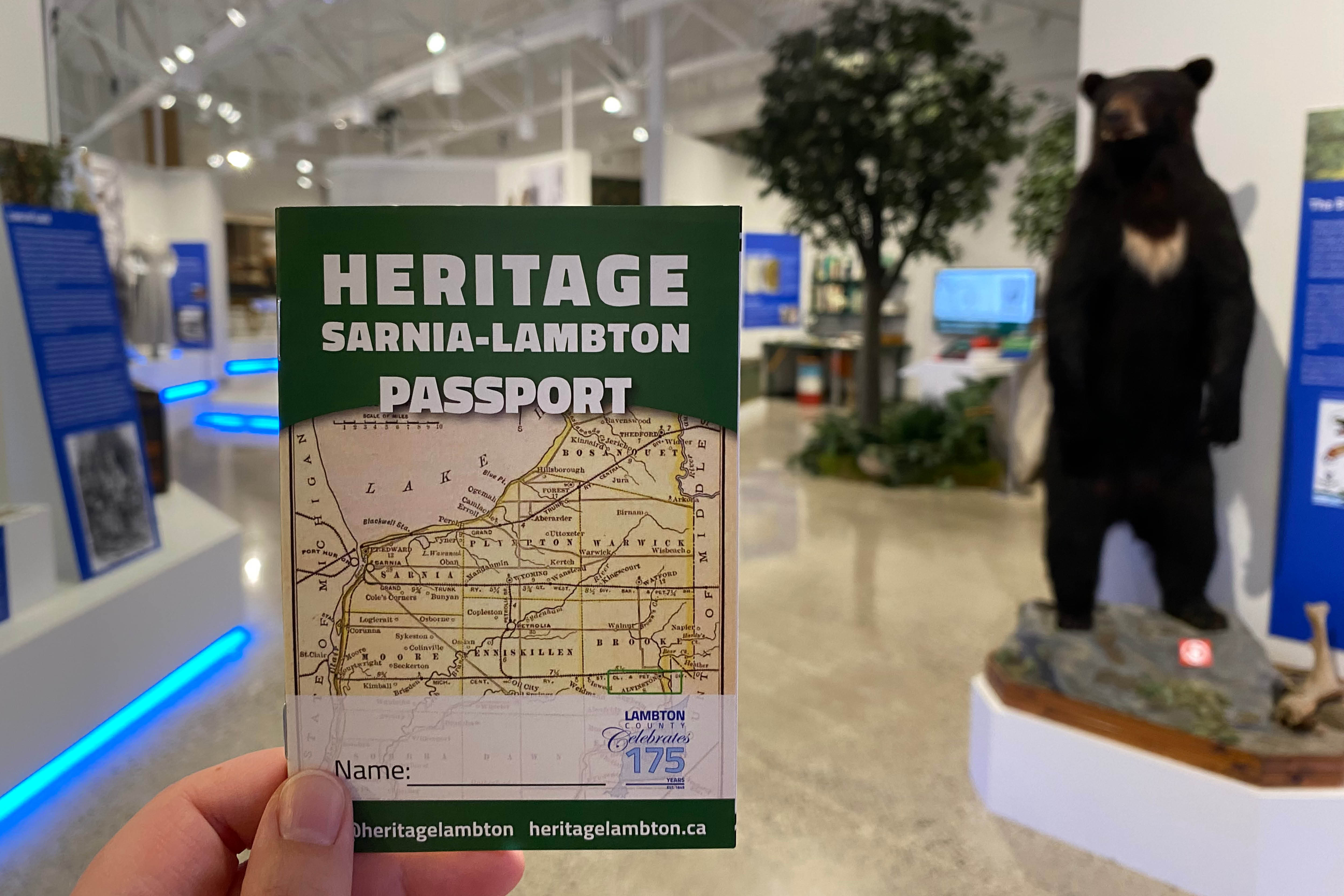 A HSL Passport booklet is held up by a human hand in front of the entrance to the Lambton Gallery in Lambton Heritage Museum.