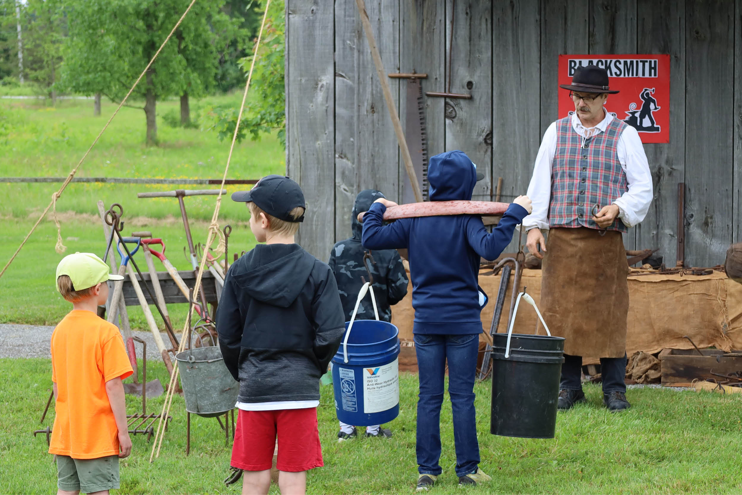 Children wait while a child tries a yoke with buckets during a historical blacksmith demonstration at Black Gold Fest.