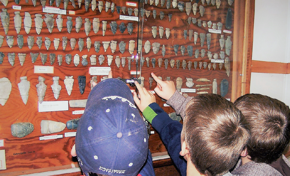 three kids pointing to artifacts hanging on a wall.