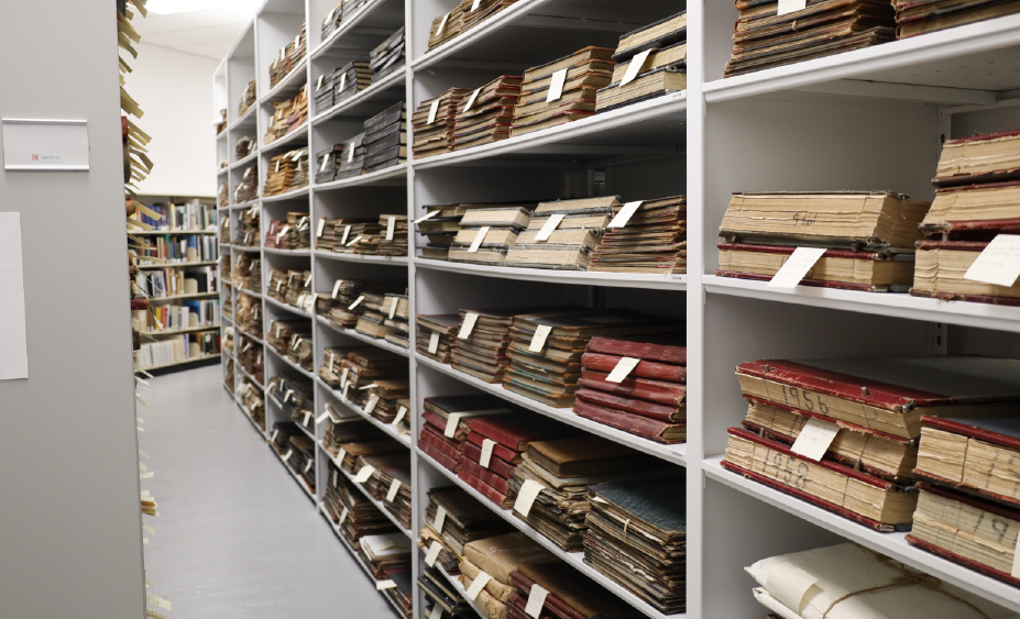 A bunch of old books and maps on white shelves.