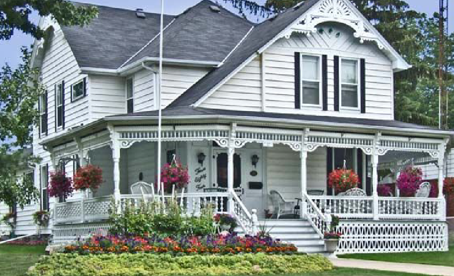 White victorian house with green yard and colourful garden beds.